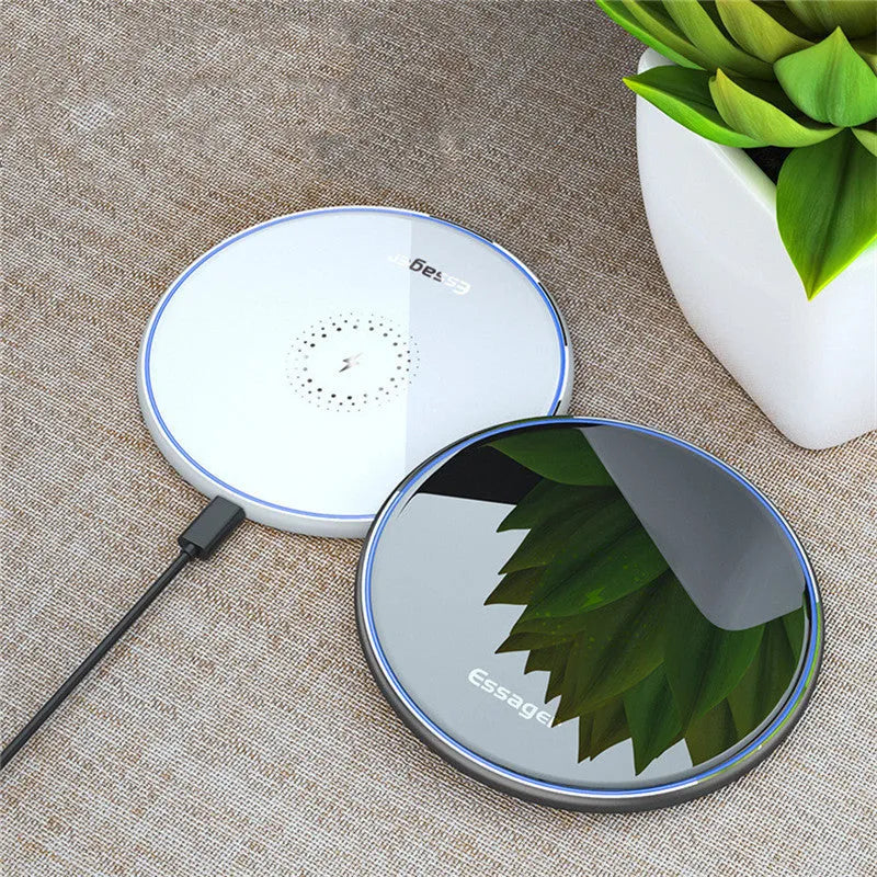 Black 15W fast wireless charging pad on a wooden desk next to a smartphone.