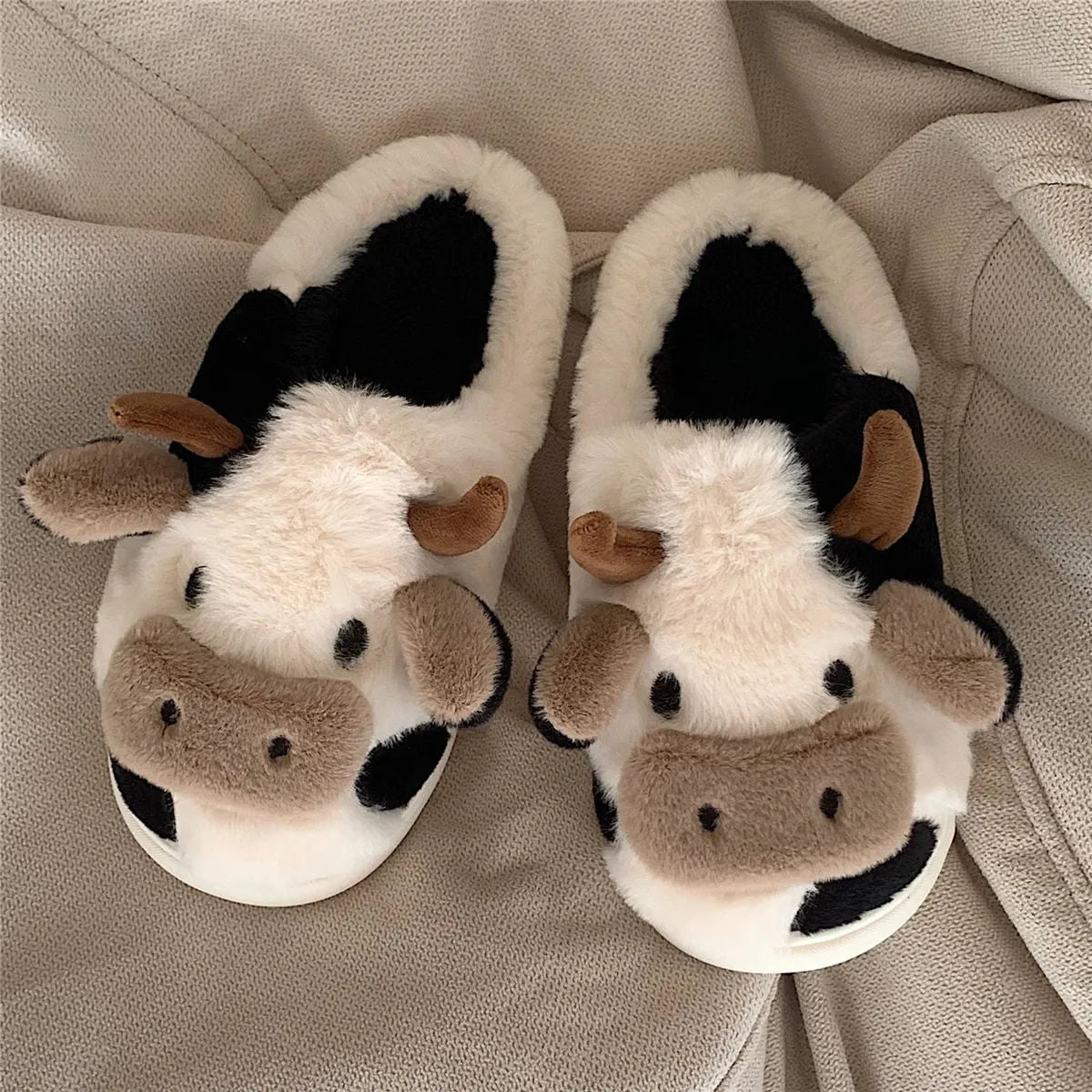 White cartoon cow plush house slippers for women with a non-slip textured sole.