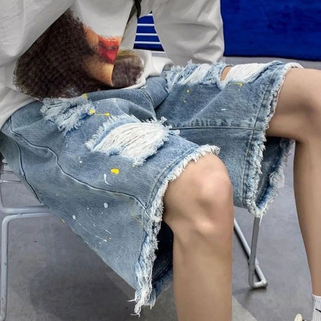 Men's loose fit light blue denim shorts with a water washed finish and hole detailing on a solid background.