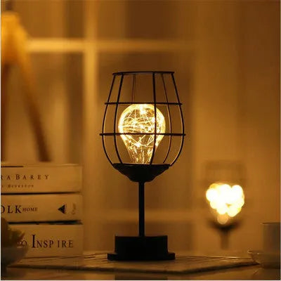 Minimalist hollow iron table lamp in red wine glass style on a wooden desk.