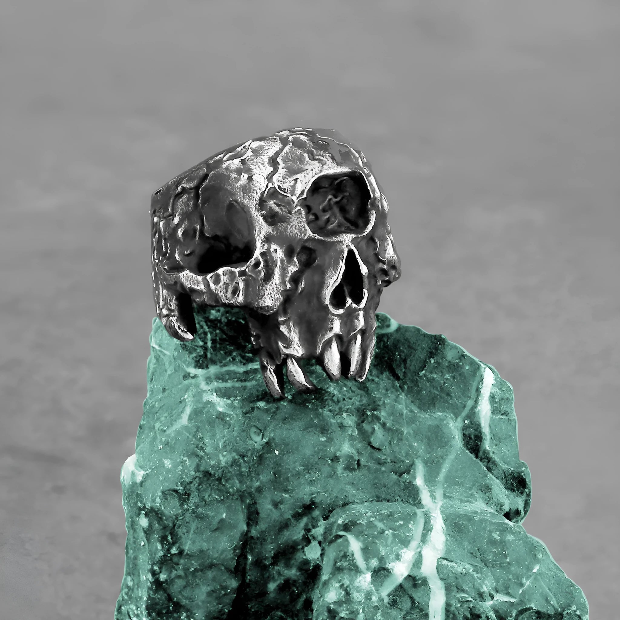 A silver-toned alloy ring with a raised one-eyed skull design on a black background.