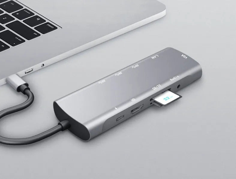 Grey aluminium USB-C docking station with HDMI, VGA, USB, and charging ports on a desk.