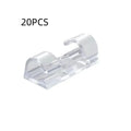 Transparent plastic self-adhesive cable clip holding a white wire against a wall.