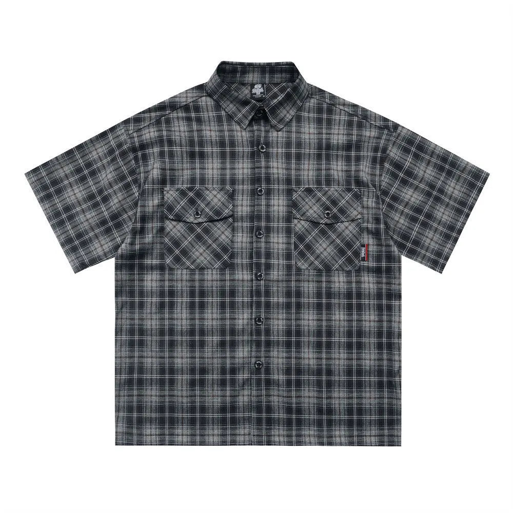 Man wearing a black and brown plaid short sleeve shirt with embroidered letter on lapel
