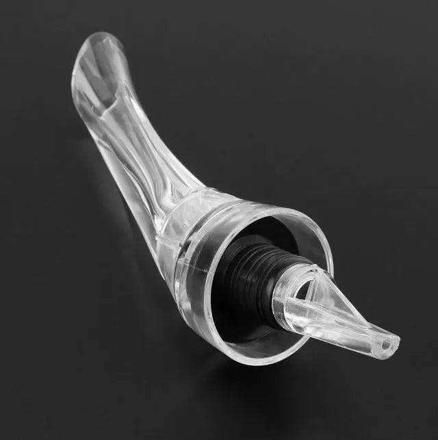 A slender, clear acrylic wine aerator pourer with a stainless steel filter inside, shown next to a wine glass.