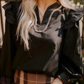 Black V-neck blouse with long ruffle sleeves and white contrast stitching.