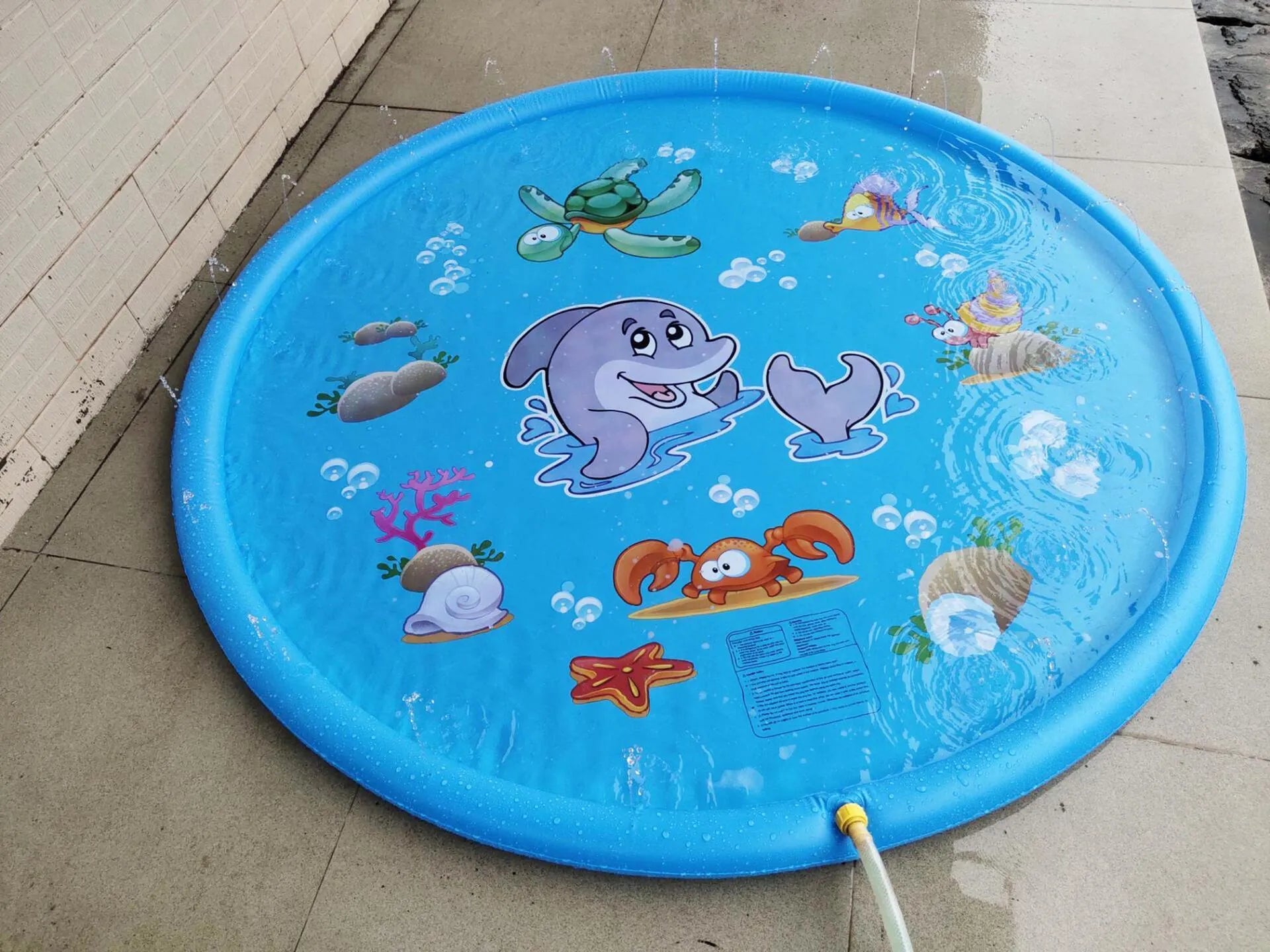 Blue PVC children's water spray play mat with marine animal print, shown on grass.