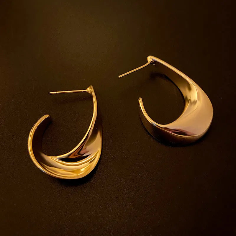 A pair of geometric twisted metal earrings with a round shape in a gold colour.