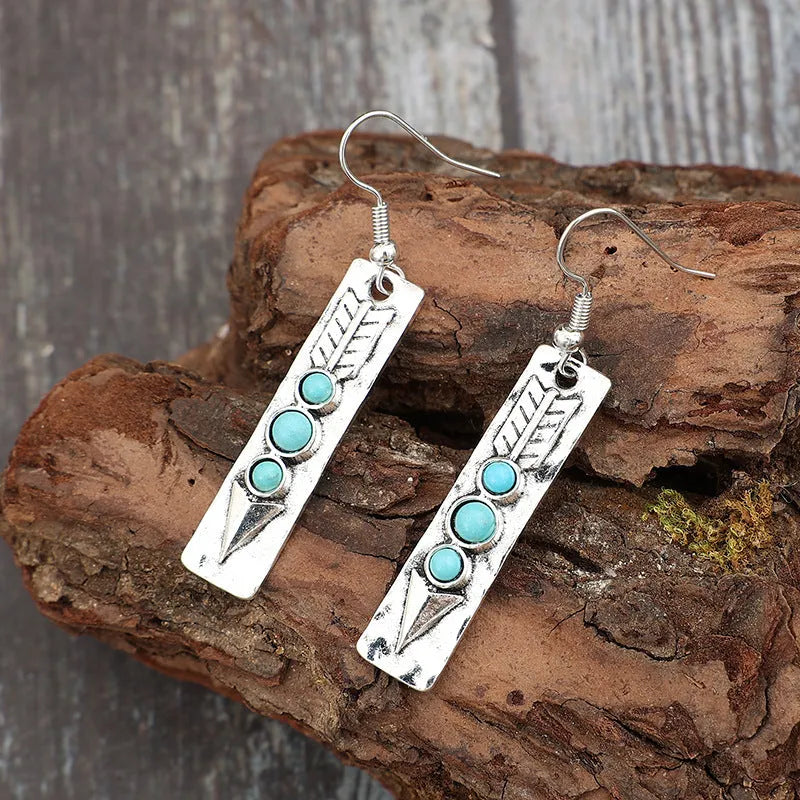 Geometric long silver earrings with blue turquoise inlay detail on a white background.