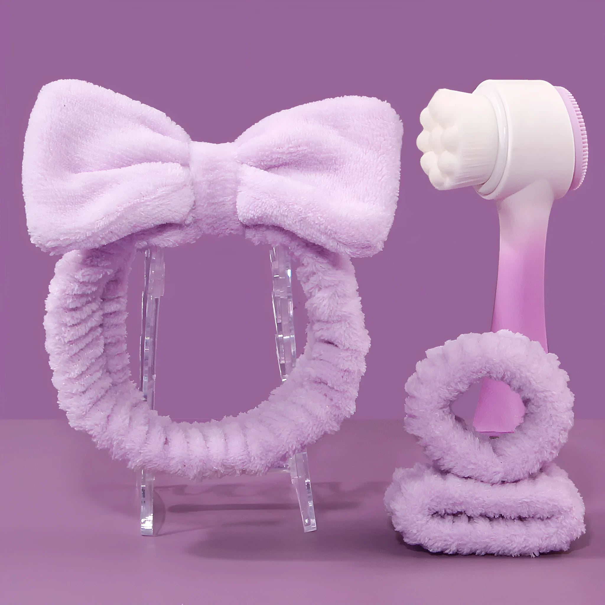 Facial brush with plastic handle and nylon bristles alongside coral fleece absorbent hair band in purple colour