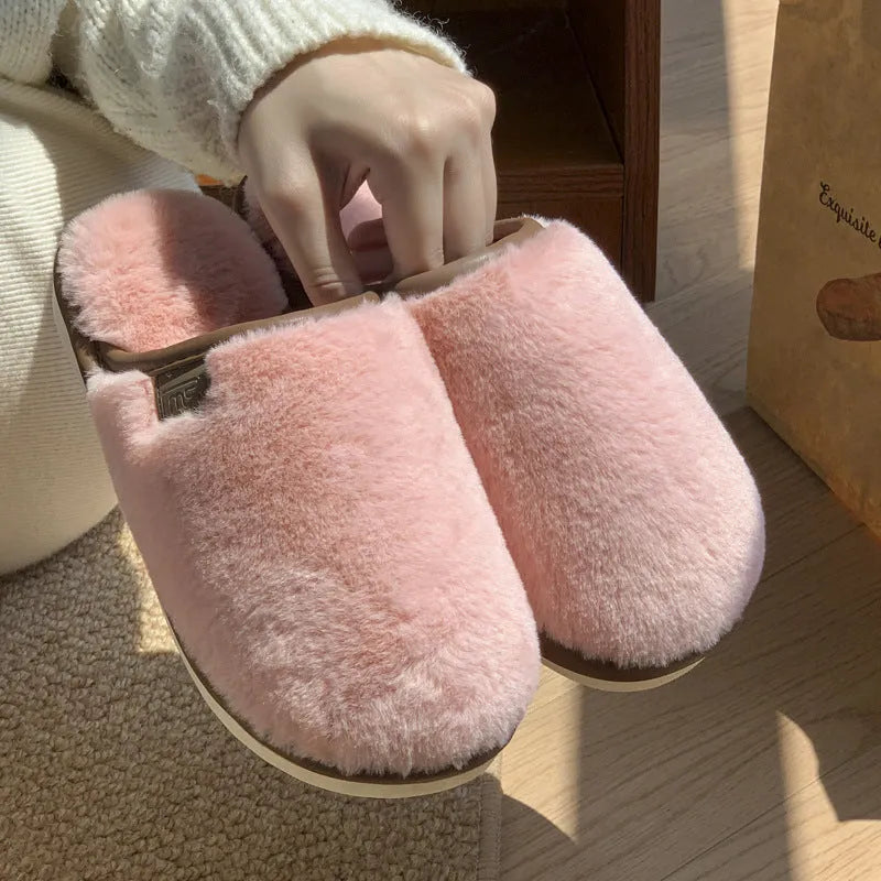 Pair of solid colour plush house slippers with PVC sole on a wooden floor.