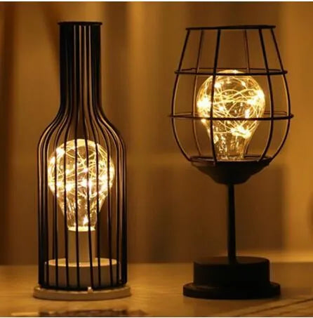 Minimalist hollow iron table lamp in red wine glass style on a wooden desk.