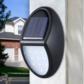 Black rectangular LED solar-powered outdoor wall light mounted on a fence.