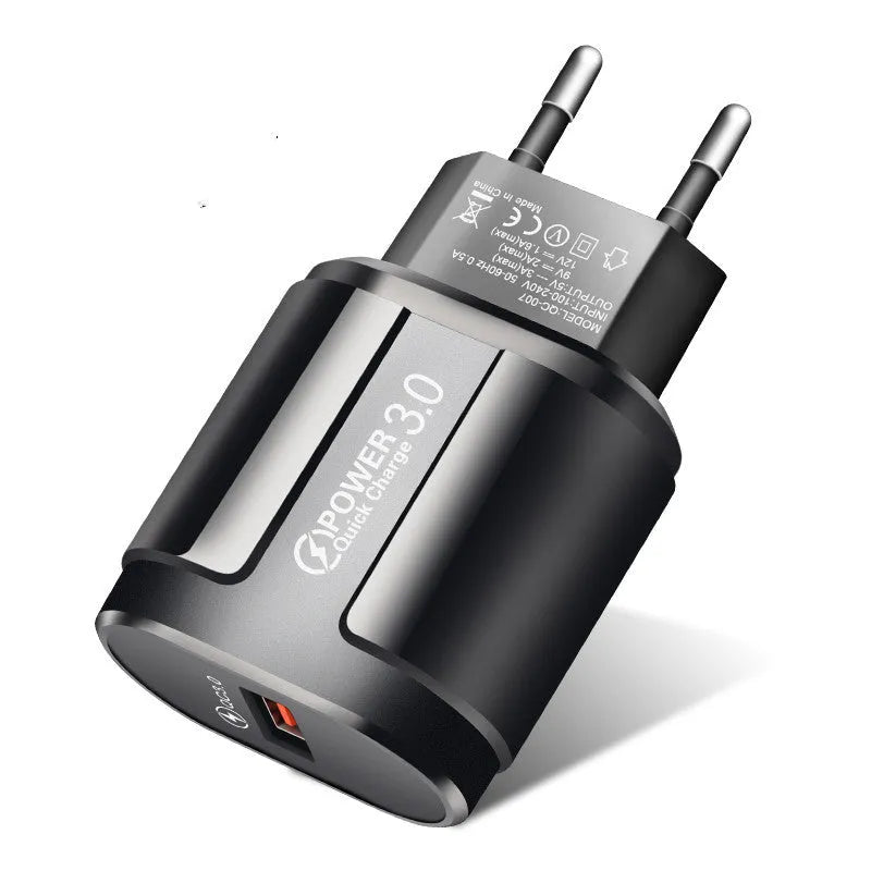 White and black mobile phone travel chargers with UK, US, and EU plug attachments on a table