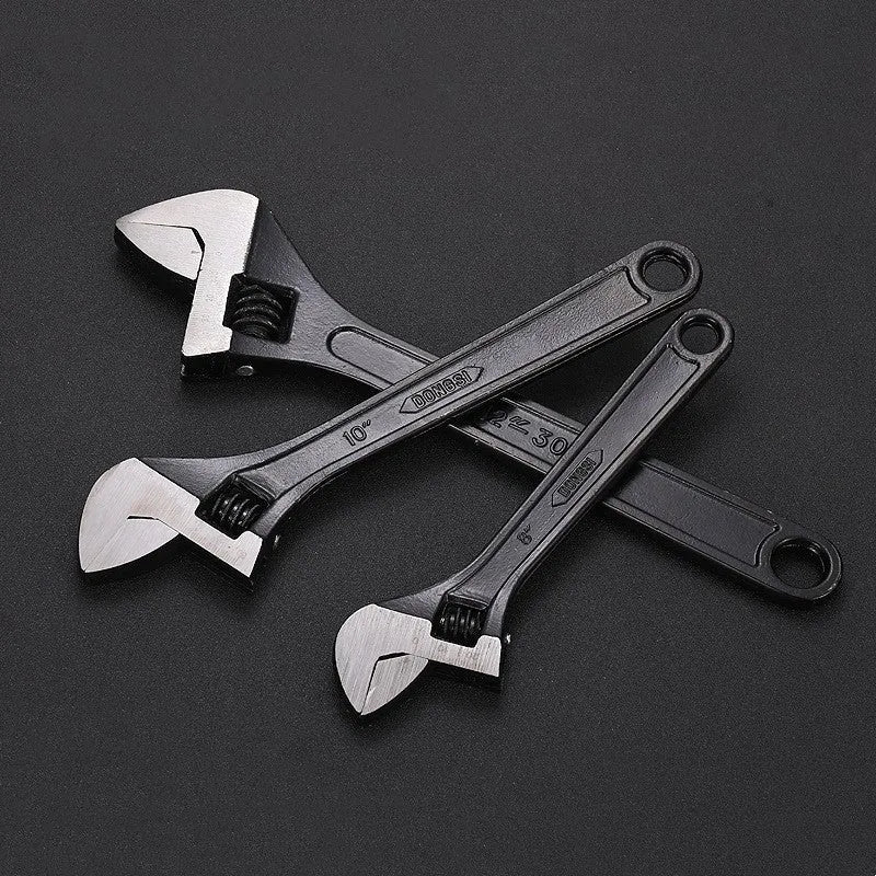 Blackened high-carbon steel adjustable open-end wrench with ergonomic handle on a workbench.