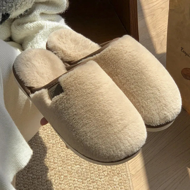 Pair of solid colour plush house slippers with PVC sole on a wooden floor.