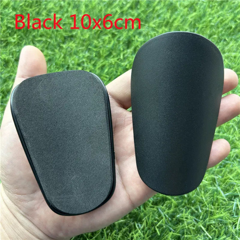 Extra small black and white plastic football shin guards for youth players, size 8cm by 5cm.