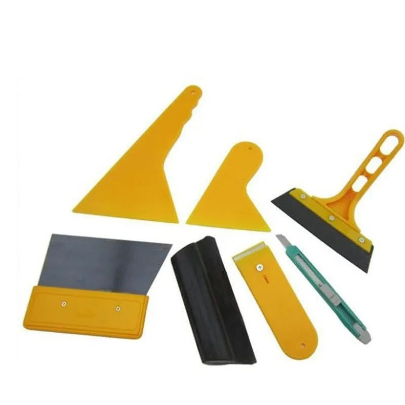 Seven-piece automotive film tool set with scrapers, knives, and a pressing block on a work surface.