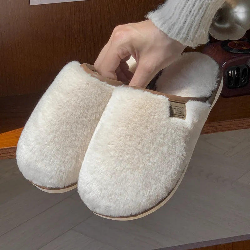 Pair of solid colour plush house slippers with PVC sole on a wooden floor.