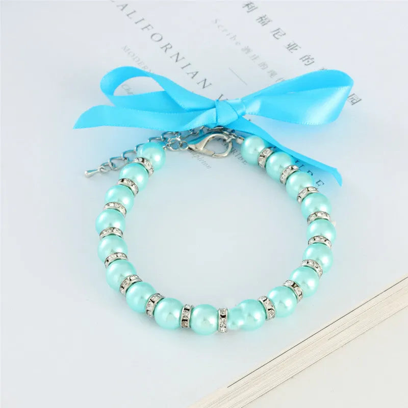 Small dog wearing a blue pearl and rhinestone necklace with a ribbon bow.