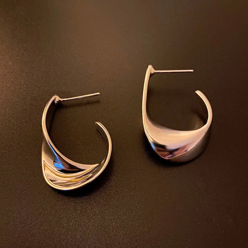 A pair of geometric twisted metal earrings with a round shape in a gold colour.