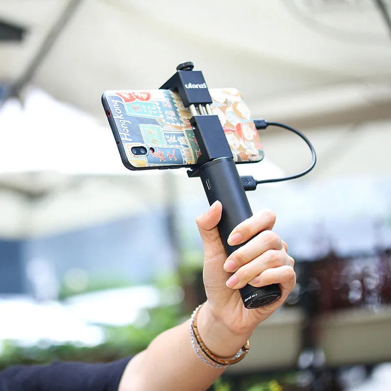 Black aluminium alloy portable power bank with handle, showing compact size next to a mobile phone for scale.