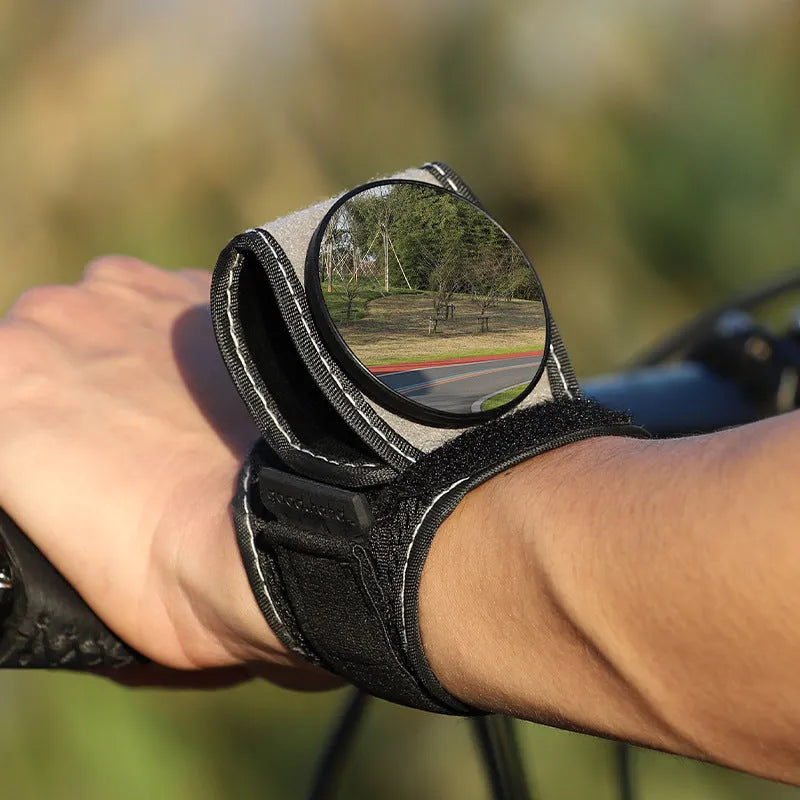 Black nylon wrist-mounted rear-view mirror for cyclists and motorcyclists on a textured background.