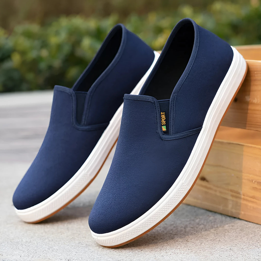 Men's low-top slip-on canvas shoe in blue on a white background, showing round toe and shallow mouth design.