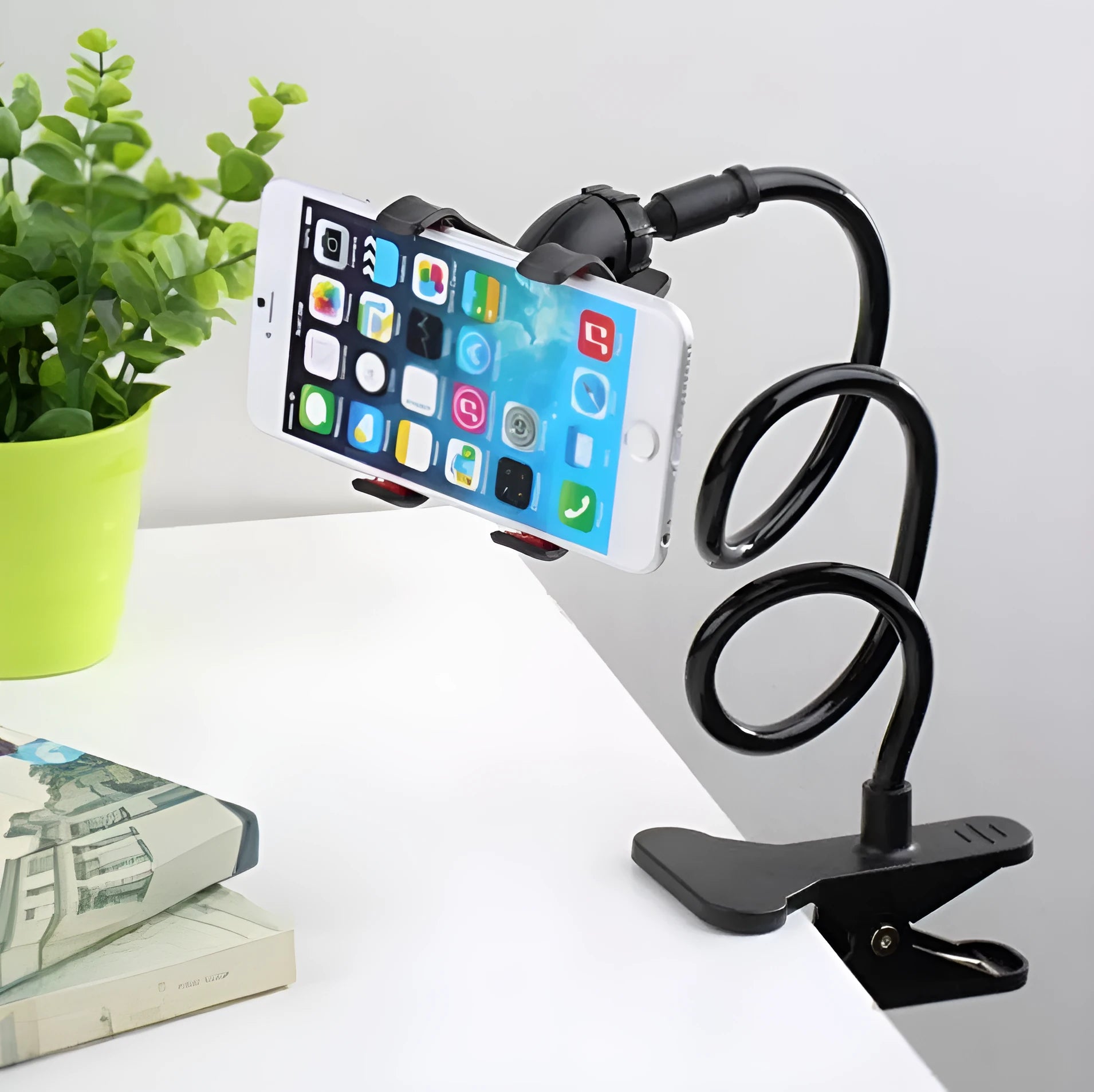 Black portable phone holder with a long flexible arm and a V-shaped clip, extended on a bedside table.