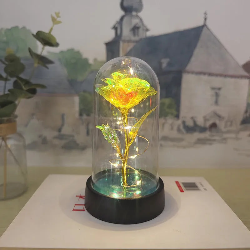 Small decorative table lamp with coloured LED lights illuminating plastic flowers under a glass dome.