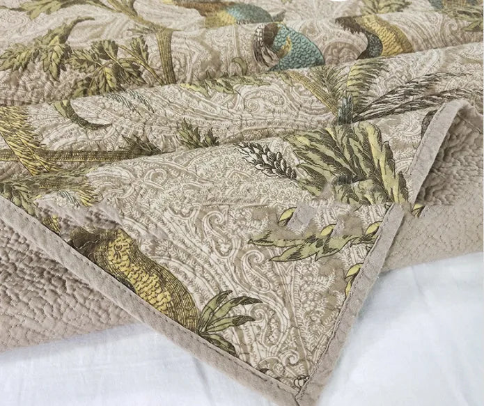Blue cotton quilted bedspread with detailed floral and bird pattern, shown on a bed.