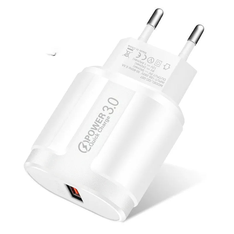 White and black mobile phone travel chargers with UK, US, and EU plug attachments on a table