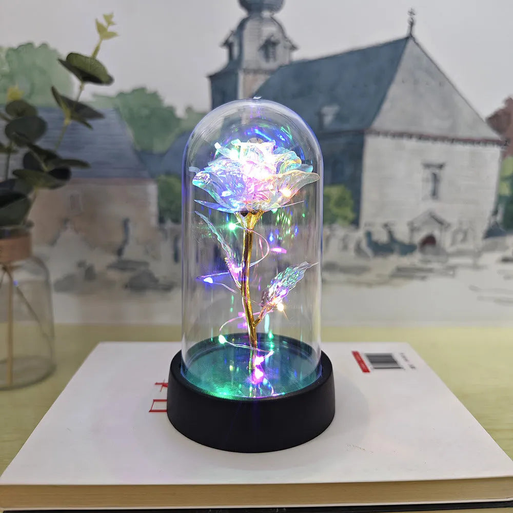 Small decorative table lamp with coloured LED lights illuminating plastic flowers under a glass dome.