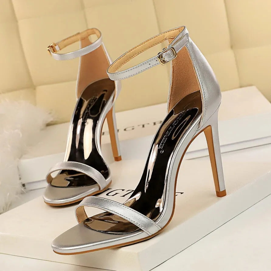 Women's ankle-strap high heel sandals in an open-toe design, showing buckle detail and available in multiple colours.