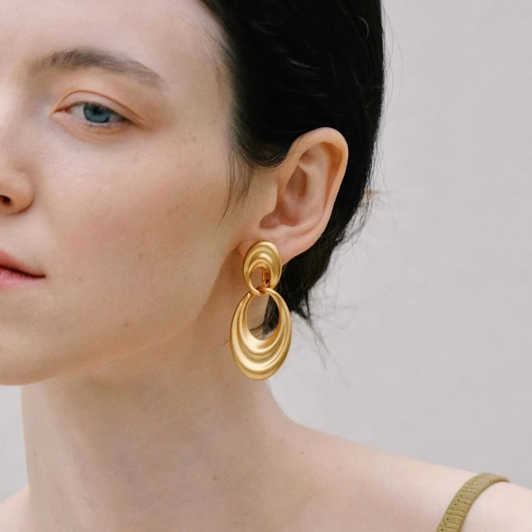 Pair of quicksand gold copper earrings showing a U-shaped design with a double circle detail.