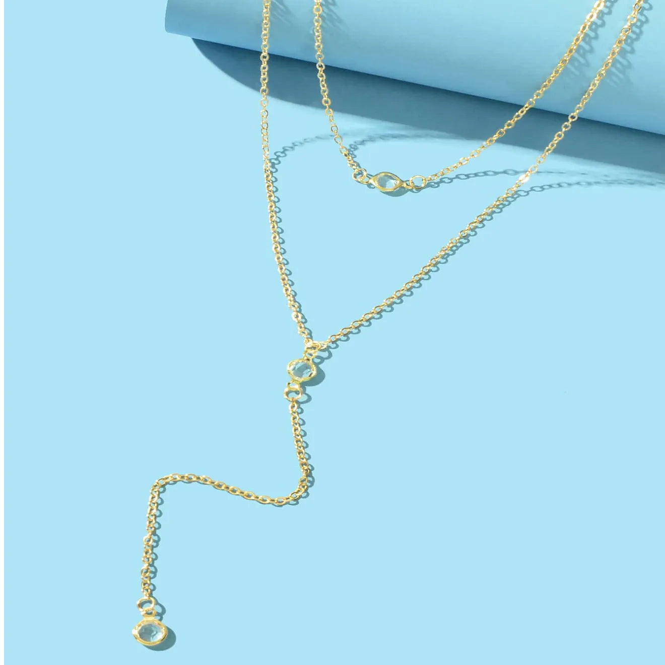 Female gold alloy O-ring chain necklace with geometric pendant on a light background
