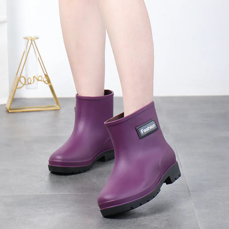 Women's mid-calf PVC rain boot in black on a wet surface, showing low heel and clean design.
