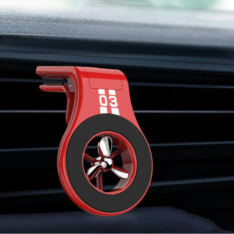 Black magnetic car phone holder clipped to a car air vent, showing adjustable paddle and fragrant slice.