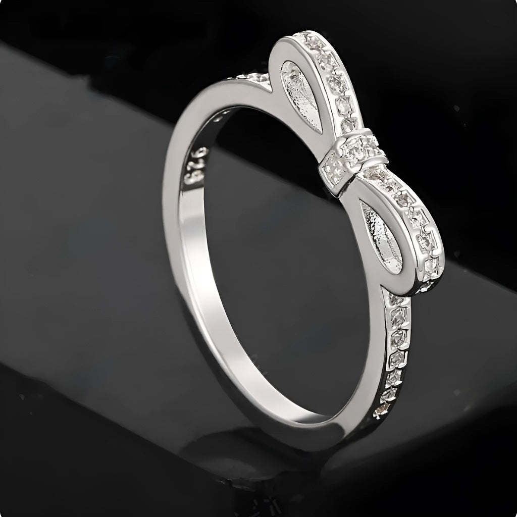Silver coloured bow-shaped ring with zircon crystal details on a white background.