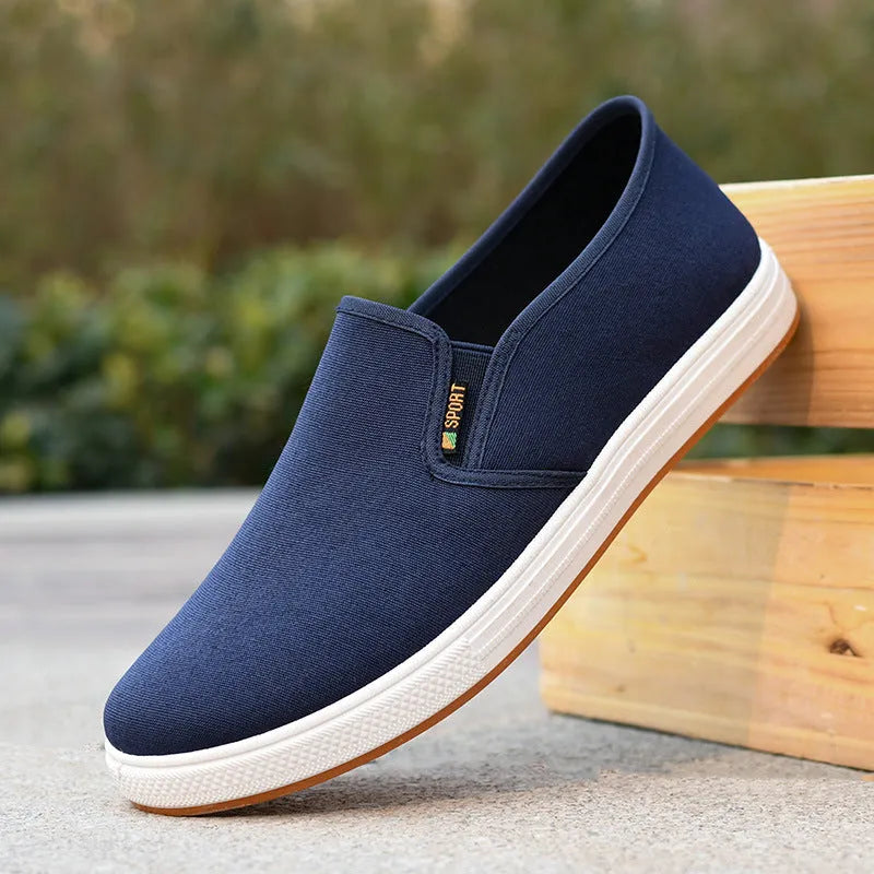 Men's low-top slip-on canvas shoe in blue on a white background, showing round toe and shallow mouth design.