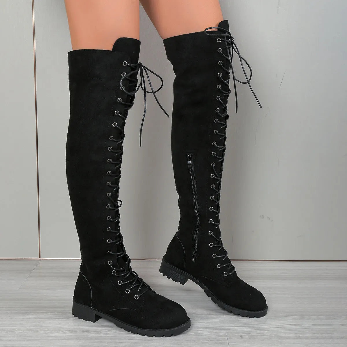 Black lace-up over-the-knee boots with a round toe and flat rubber sole on a neutral background.