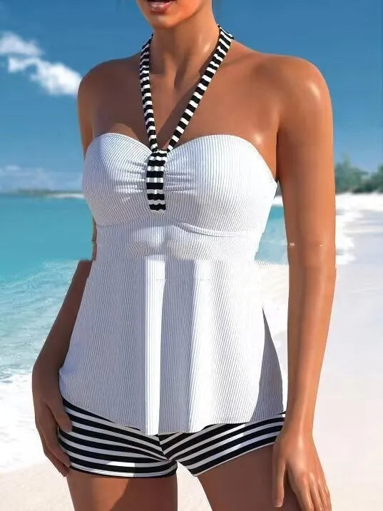 Woman modelling a black and white striped off-shoulder one-piece swimsuit on a beach.
