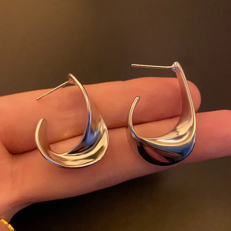 A pair of geometric twisted metal earrings with a round shape in a gold colour.