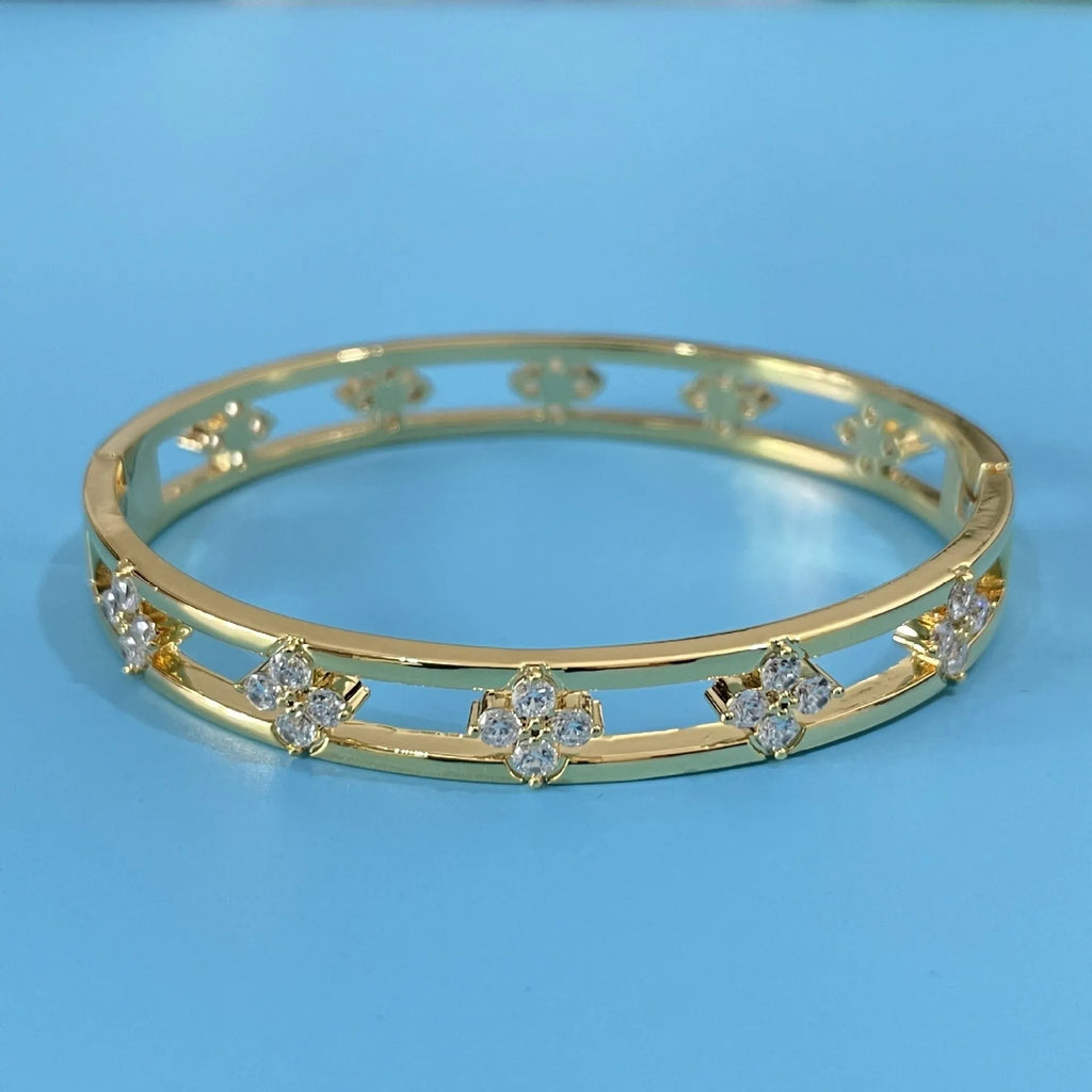 Gold and silver women's hollow bracelets with zircon stones and four-leaf clover charms on a white background.