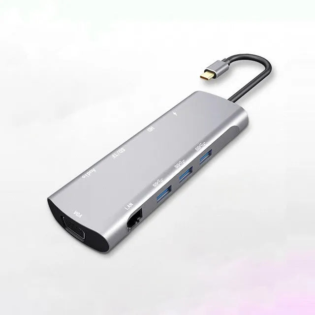 Grey aluminium USB-C docking station with HDMI, VGA, USB, and charging ports on a desk.