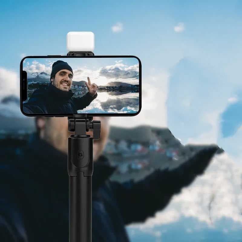 Black Bluetooth selfie stick with extended tripod legs and a phone mounted in its 360-degree rotating holder.
