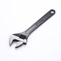 Blackened high-carbon steel adjustable open-end wrench with ergonomic handle on a workbench.