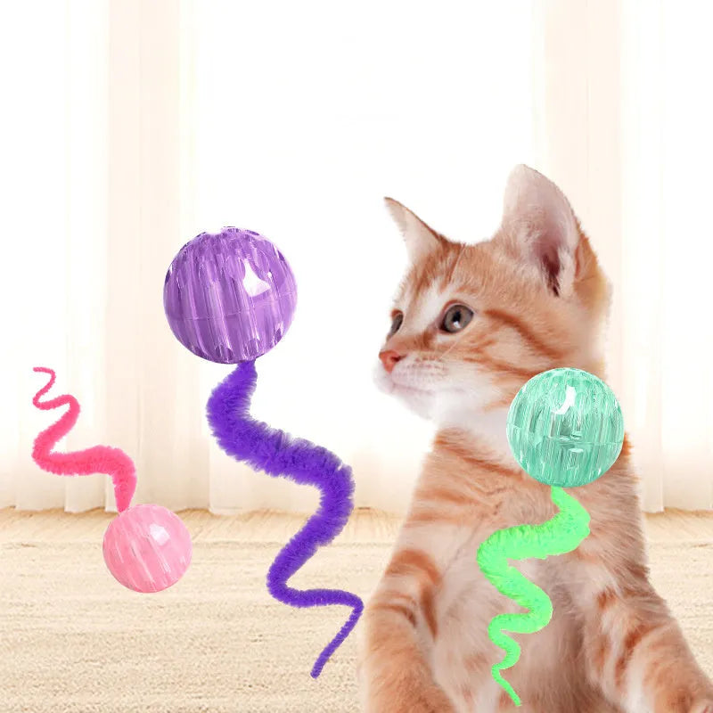 Green TPR bouncy ball with pink plush worm tail cat toy on floor