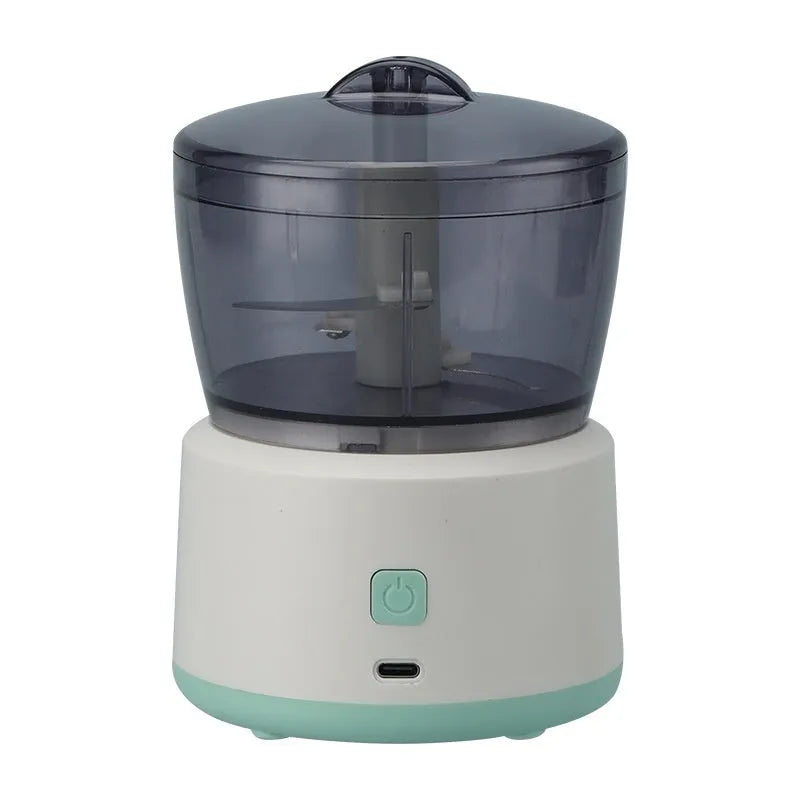Mini electric food processor in light green with transparent cup and stainless steel blades on countertop.