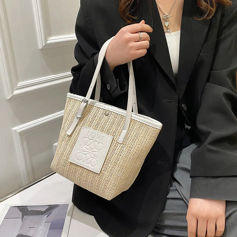 Women's straw woven shoulder bag with PU trim showing tapered shape and sewn thread details